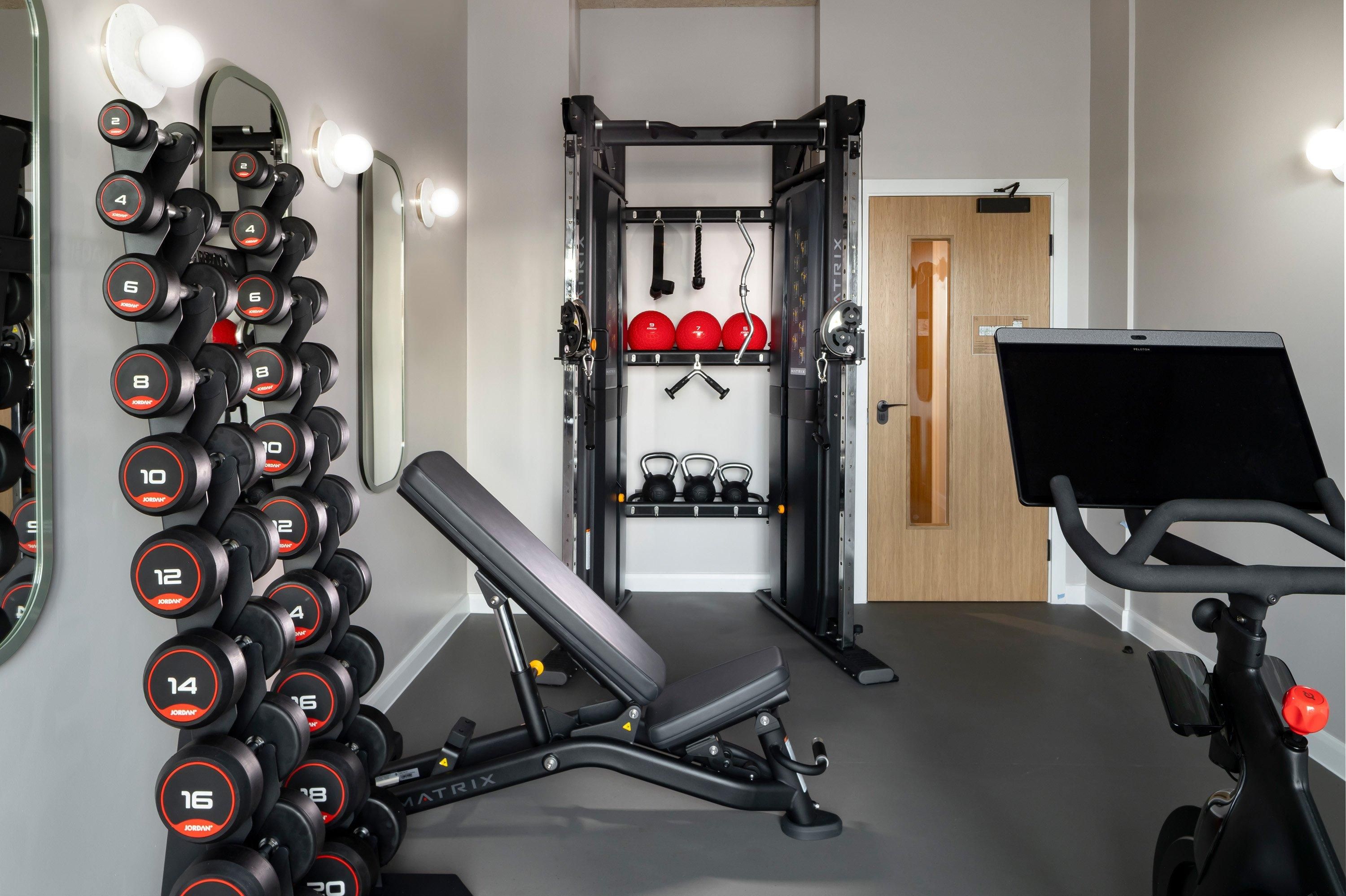 Un gimnasio con una banca, mancuernas, kettlebells y una bicicleta estática.