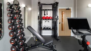 Un gimnasio con una banca, mancuernas, kettlebells y una bicicleta estática.