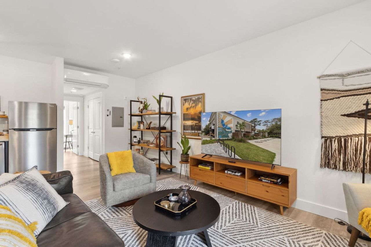 Un salon moderne avec un canapé, une table basse et un téléviseur posé sur un meuble en bois. On y trouve également une bibliothèque et un tableau accroché au mur.