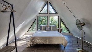 A bedroom with a large window, a bed, a standing fan, and a clothes rack. - 4BR/3BA Cabin w/ Games & Hot Tub, Near Smoky Mtns (Kodak)