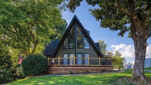 A cabin with a triangular roof, a wooden deck, and a view of a tree and sky. - 4BR/3BA Cabin w/ Games & Hot Tub, Near Smoky Mtns (Kodak)
