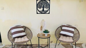 Deux fauteuils en osier avec des coussins à rayures, une petite table avec une plante et une œuvre d’art accrochée au mur.