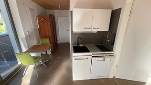Una kitchenette compacta con un lavamanos, una pequeña encimera y un lavavajillas pequeño. Hay una zona de comedor con una mesa y dos sillas.