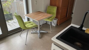 Una cocina pequeña con una mesa de madera y dos sillas verdes, un lavamanos negro y vistas al balcón exterior.