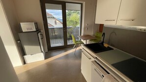 Una cocina compacta con microondas integrado, un lavamanos y un pequeño comedor con una silla.