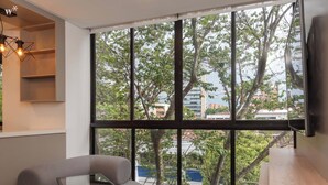 A modern room with a large window, a grey sofa, a small table, and a wooden shelf. - Ganesh by Wynwood House (Medellín)