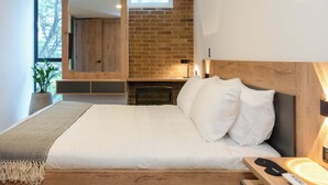 A modern bedroom with a large bed, a wooden headboard, a brick wall, and a large mirror. - Ganesh by Wynwood House (Medellín)