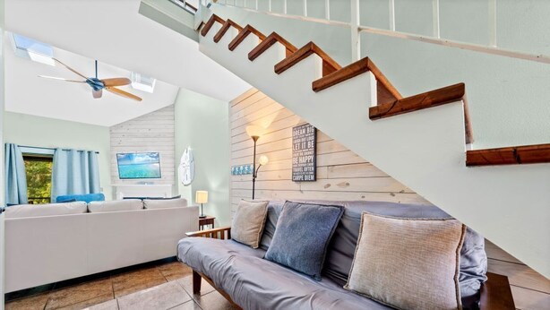 Ein modernes Wohnzimmer mit grauem Sofa, einer Holztreppe und einem Deckenventilator.