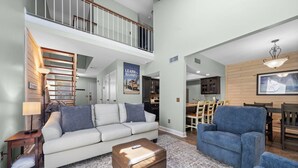 Ein geräumiges Wohnzimmer mit hoher Decke, einer Treppe, einem Essbereich und einer Küche.