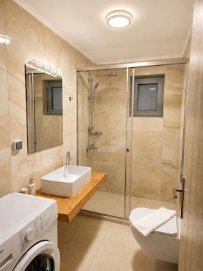 A modern bathroom with a glass-enclosed shower, a white sink, and a built-in washing machine.