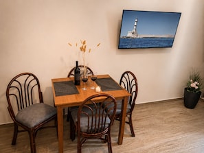 Une table à manger avec des chaises, une bouteille de vin, des verres et une bougie. Un tableau représentant un phare est accroché au mur.