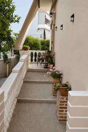 A covered outdoor area with a staircase, outdoor furniture, and potted plants.