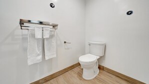 A modern bathroom with a white toilet, a towel rack with two towels, and a wooden floor. - Casablanca Inn (Bell Gardens)