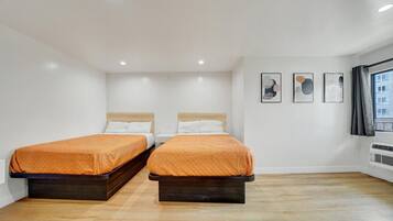 A hotel room with two beds, white walls, and a wooden floor.
