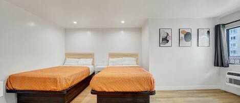 A hotel room with two beds, white walls, and a wooden floor.