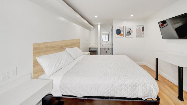 A modern hotel room with a large bed, a bedside table, a flat-screen TV mounted on the wall, and a small bathroom area visible in the background. - Casablanca Inn (Bell Gardens)