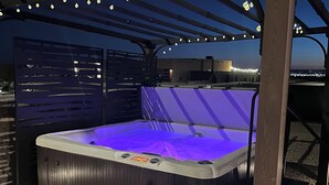 A hot tub under a pergola with string lights, surrounded by a gravel area. - Book a Winter Stay! Hot Tub & Brand New Modern Cozy Home (Las Cruces)