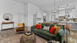 A modern living room with a green sofa, wooden chair, and a round coffee table. - Book a Winter Stay! Hot Tub & Brand New Modern Cozy Home (Las Cruces)