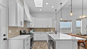 A modern kitchen with white cabinetry, a central island, and pendant lighting. - Book a Winter Stay! Hot Tub & Brand New Modern Cozy Home (Las Cruces)
