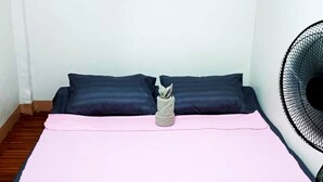 A single bed with a pink bedspread, two dark pillows, and a folded towel on the bed. A black fan is on the floor to the right. - Transient House Baguio Near Minesview With Backyard (Itogon)