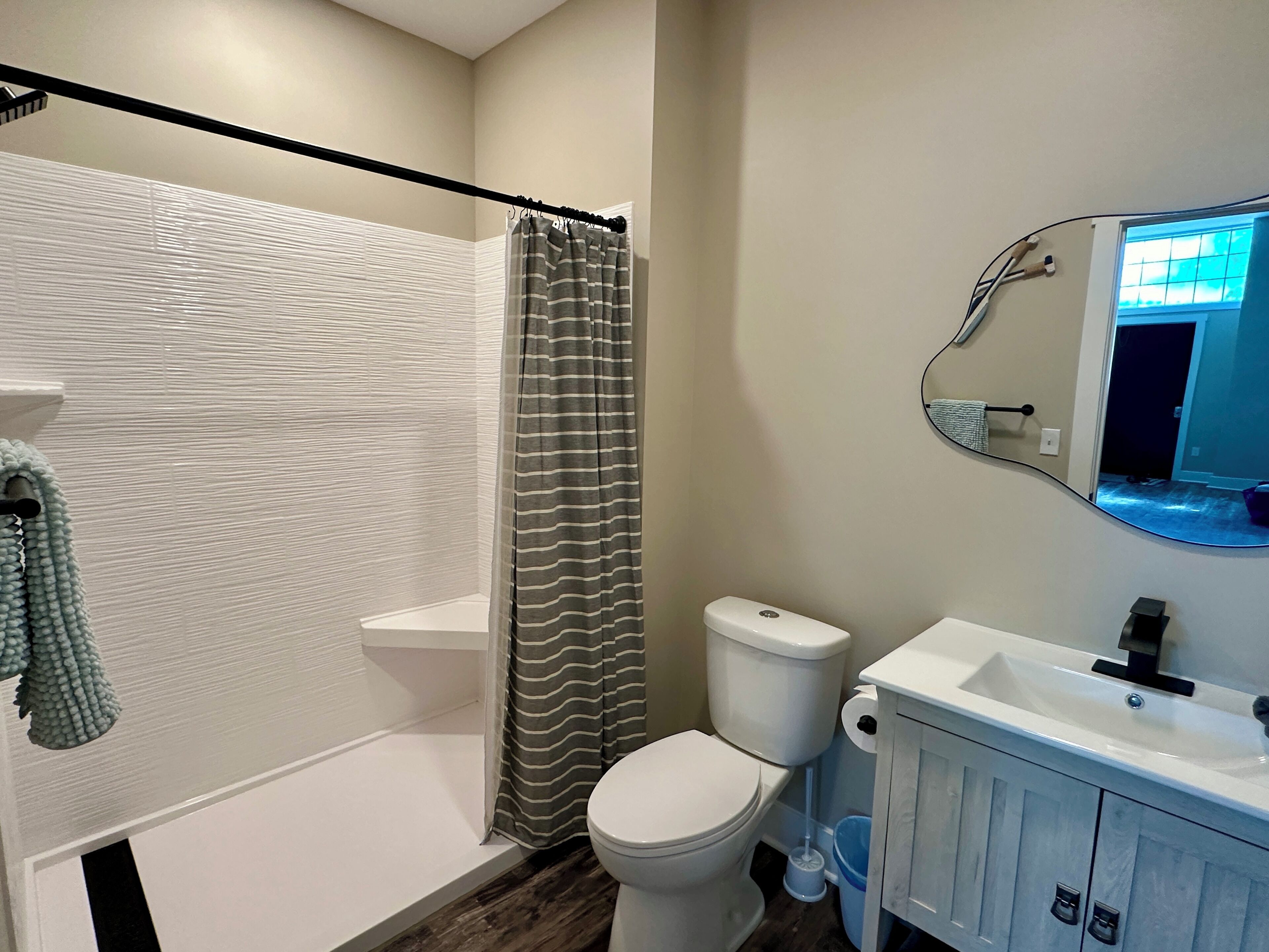 A bathroom with a shower, toilet, sink, and a mirror.