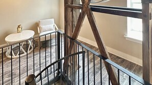 Ein rustikales Interieur mit freiliegenden Holzbalken, einer großen Zahnradmaschine, einem weißen Stuhl und einem kleinen runden Tisch mit einer Lampe.