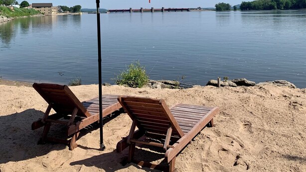 Ein Strand mit zwei Holzliegen und einem roten Sonnenschirm.