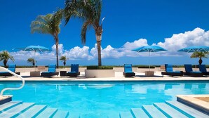 En swimmingpool med liggestole og parasoller, omgivet af palmer.
