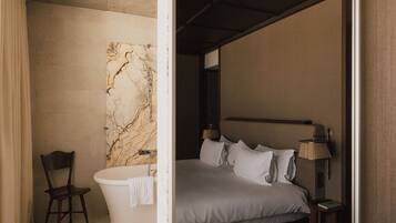 A modern bedroom with a large bed, a marble wall, a chair, and a bathtub.