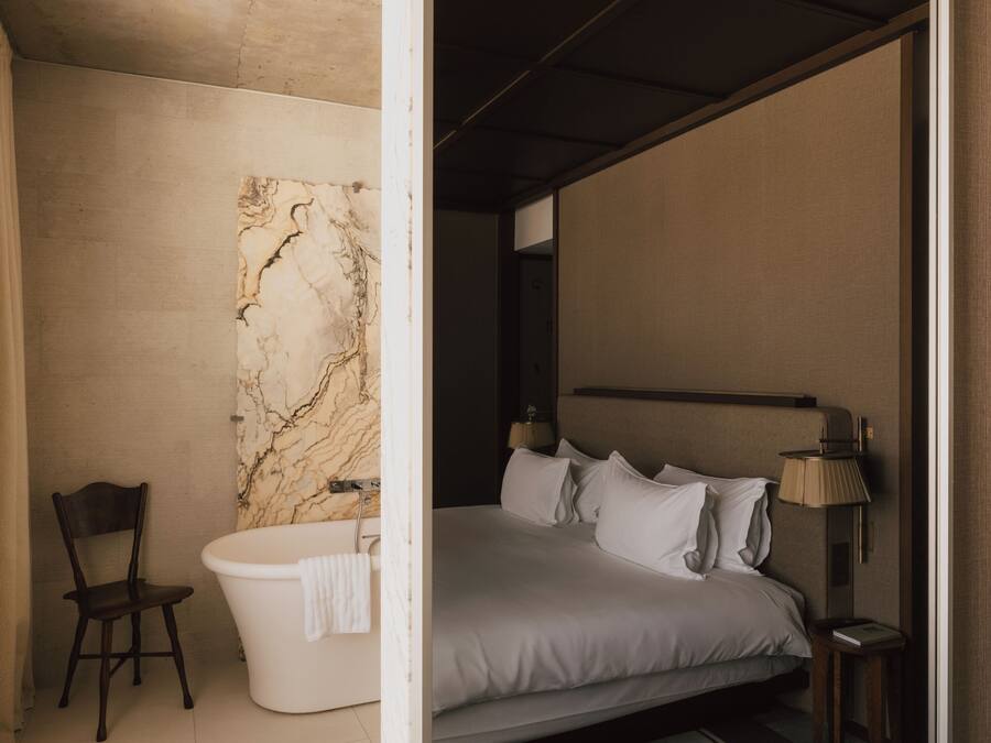 Un dormitorio moderno con una cama grande, una pared de mármol, una silla y una bañera.