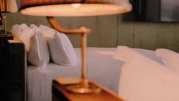 A neatly made bed with white linens and pillows, a bedside lamp, and a wooden nightstand.