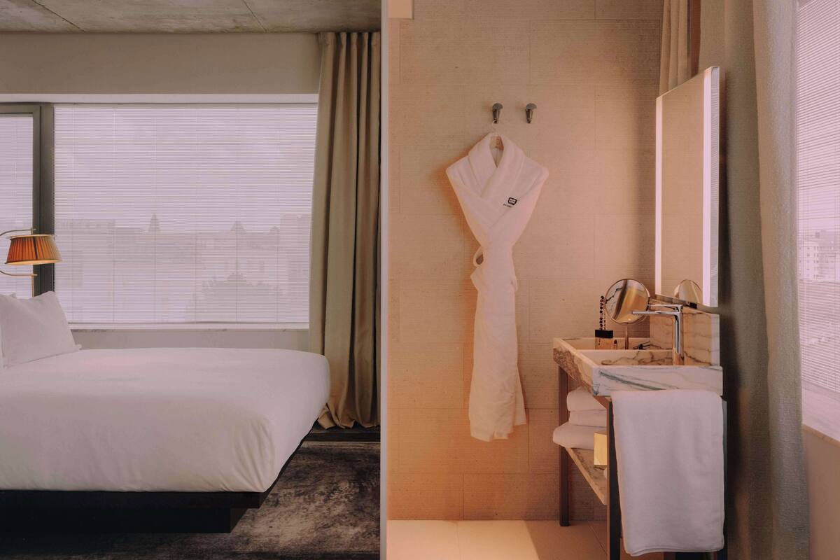 A hotel room with a bed, a bathroom with a mirror, and a robe hanging on the wall.