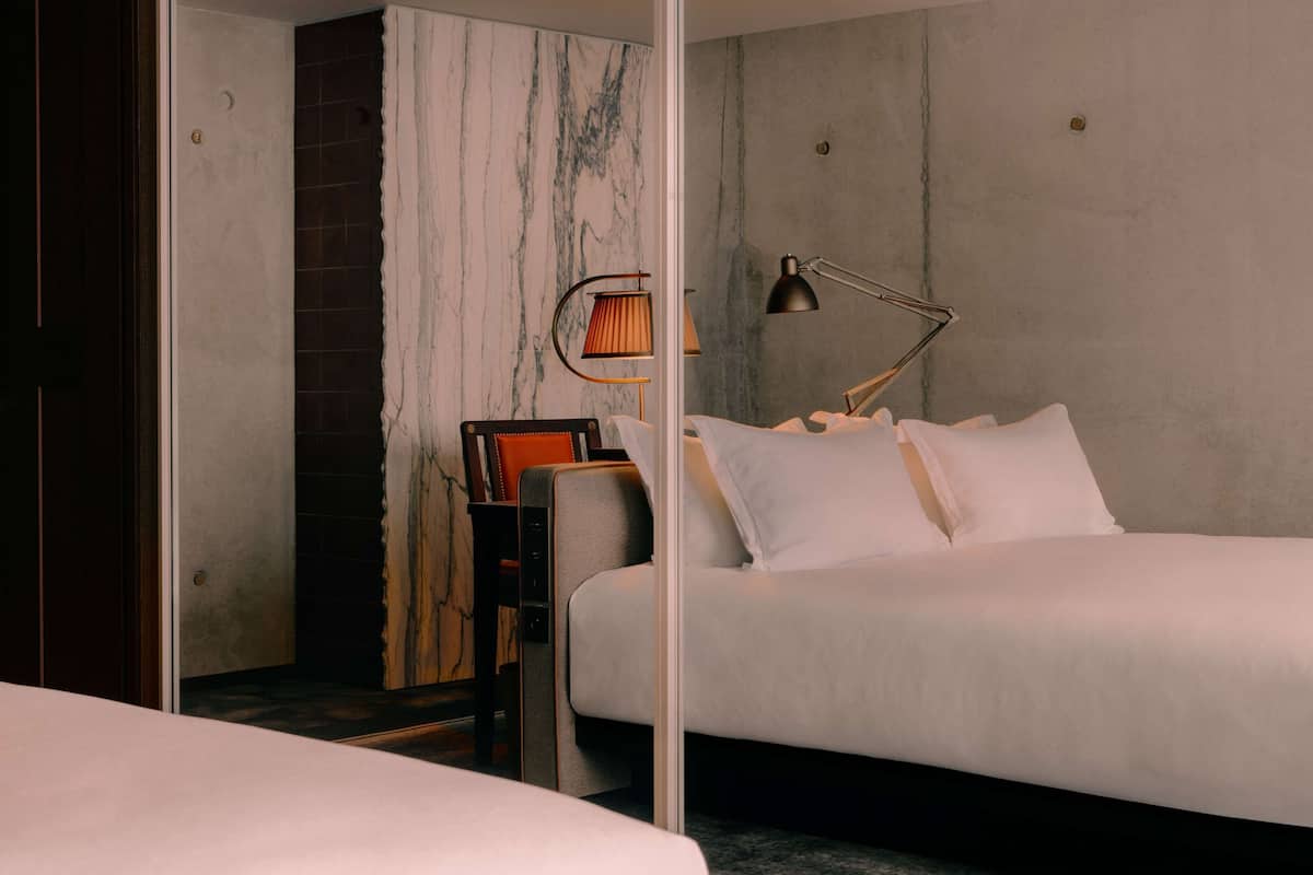 A modern bedroom with a large bed, a nightstand, a chair, and a lamp.