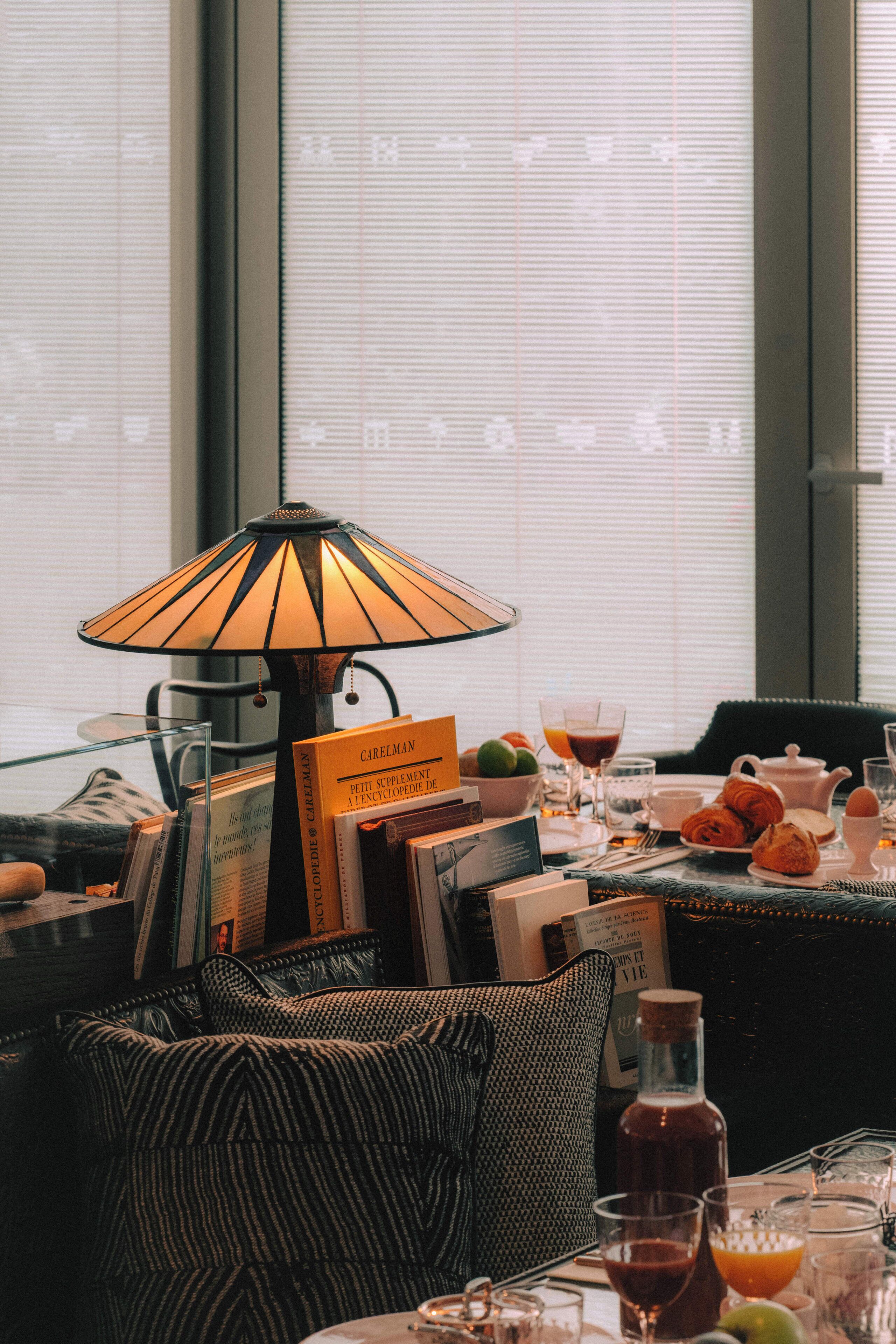 A dining area with a table set for breakfast, including books, a bottle, and a lamp.