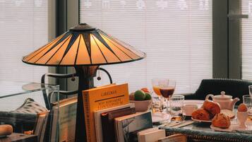 A dining area with a table set for breakfast, including books, a bottle, and a lamp.