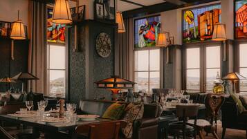 Interior de restaurante con techos altos, amplias ventanas y varias mesas dispuestas con vasos y platos.