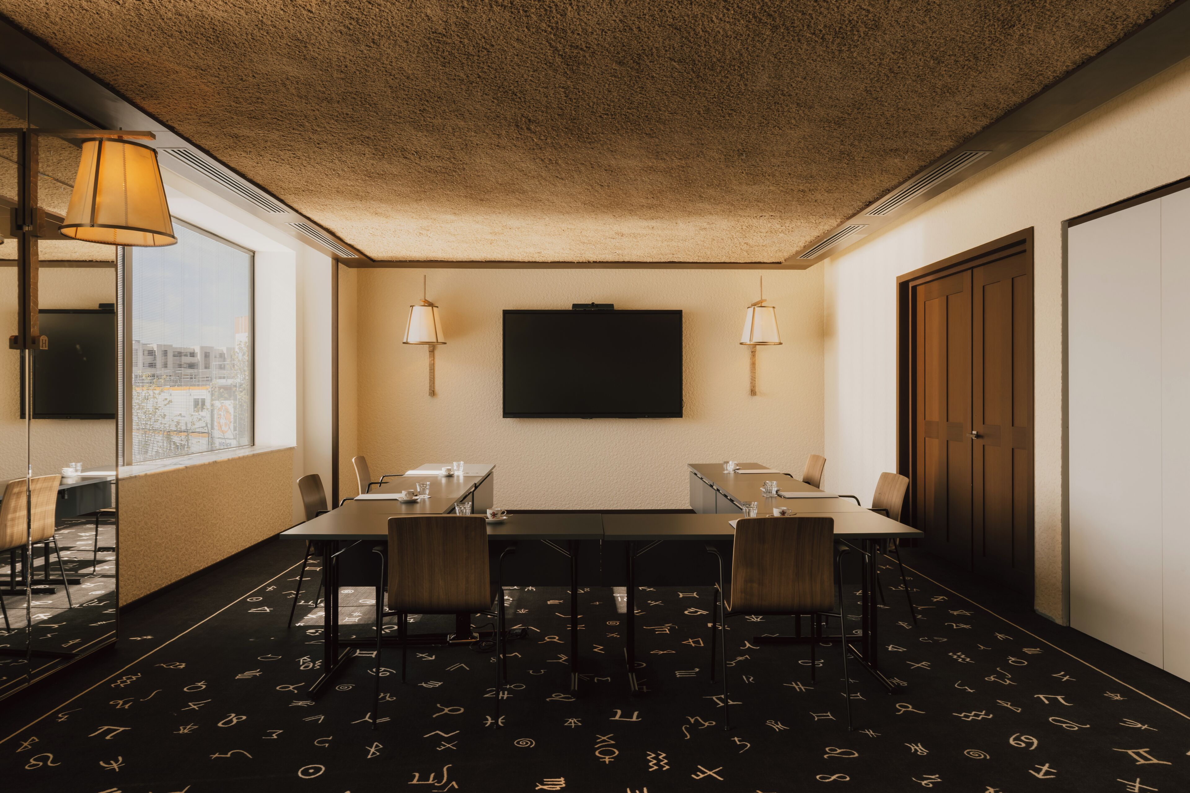 A conference room with a large table, chairs, and two wall-mounted lamps.