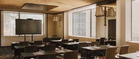 A conference room with tables, chairs, a projector screen, and large windows.