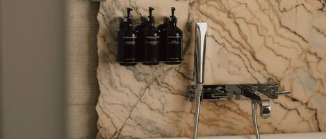 A bathroom with a marble wall, a bathtub, and a showerhead.