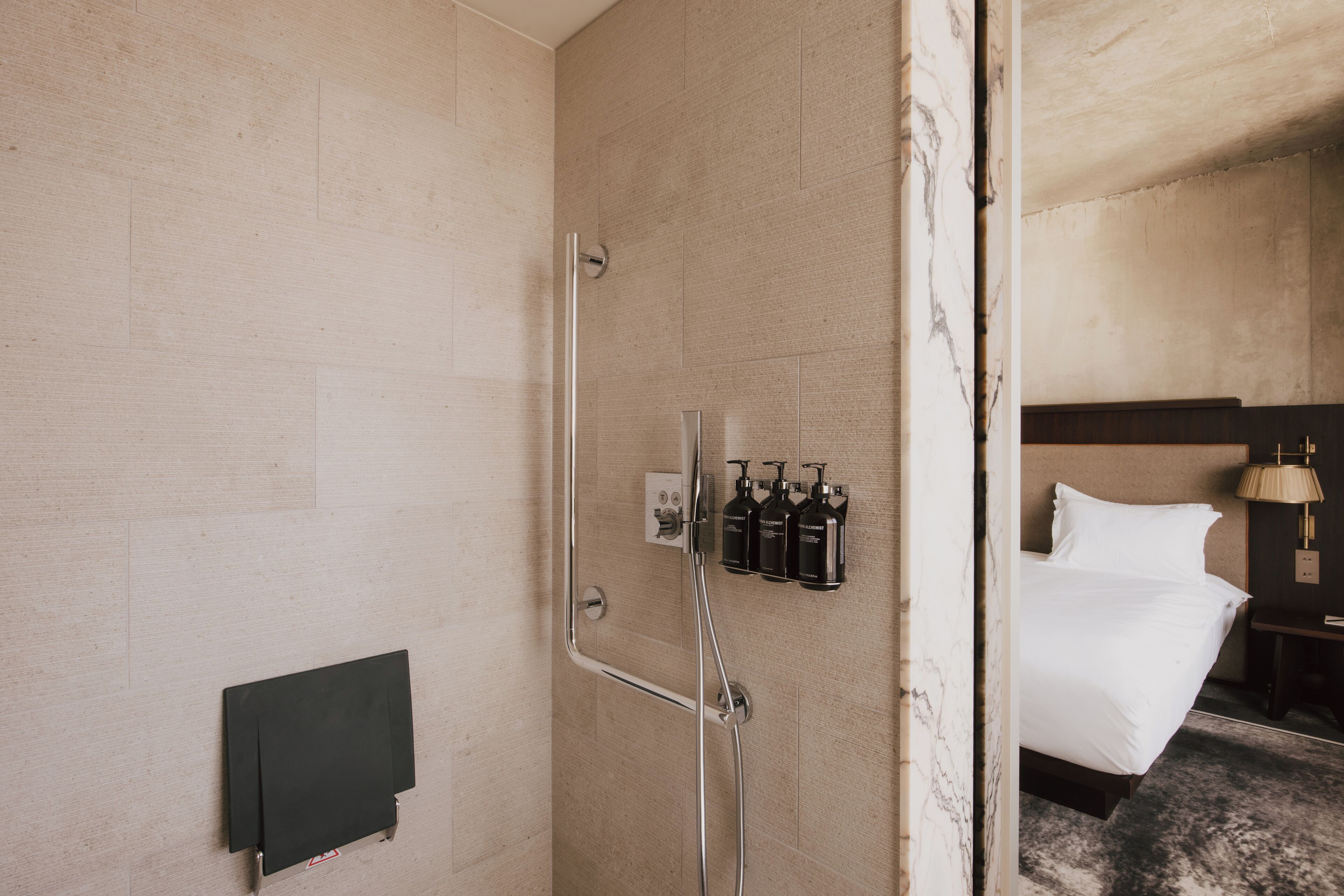 A hotel room with a shower, a bed, and a nightstand with a lamp.