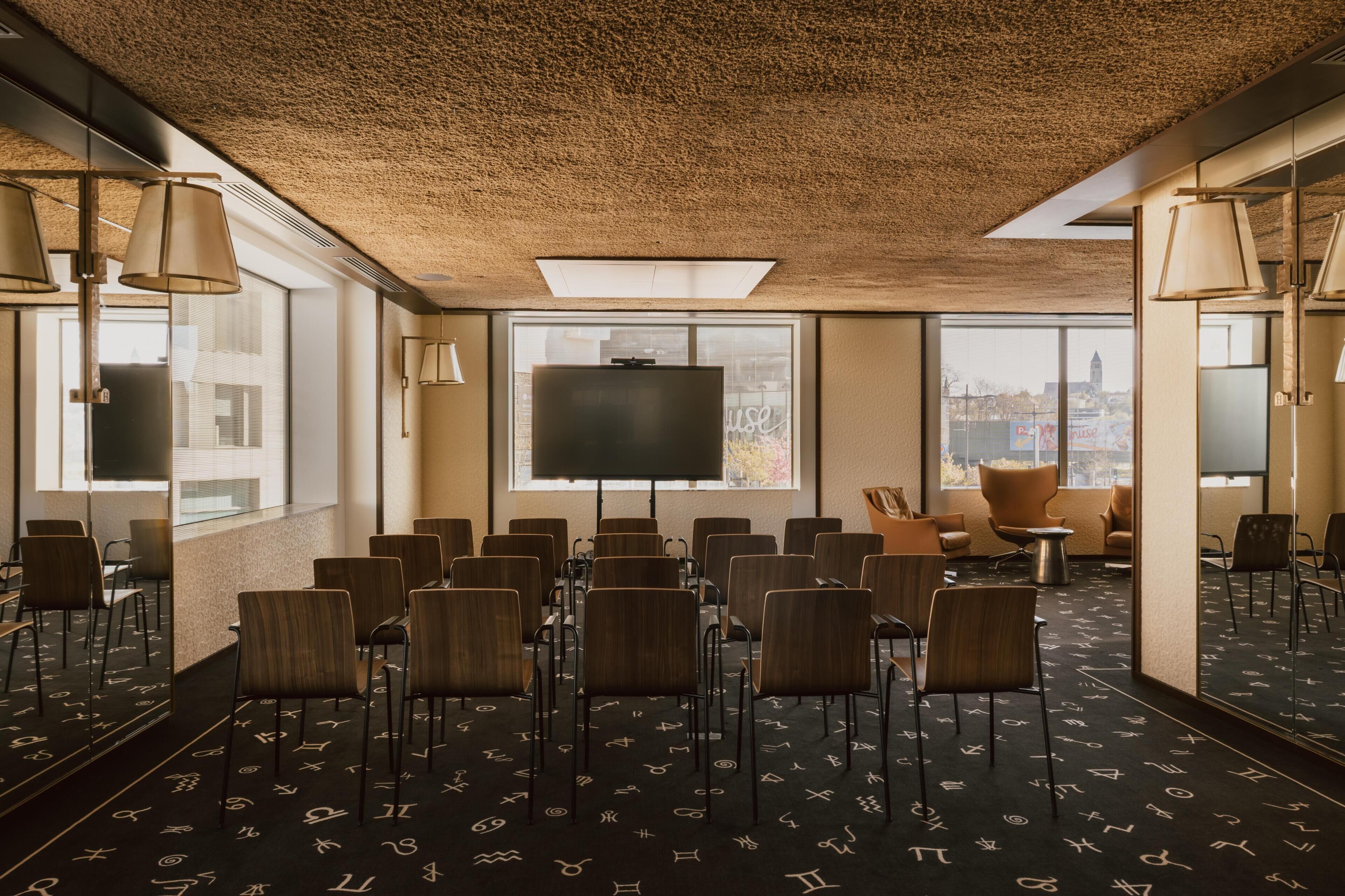 A conference room with rows of chairs, a large screen, and a city view through the windows.