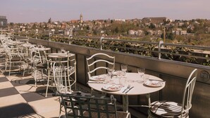 An outdoor dining area with tables and chairs, overlooking a cityscape with buildings and a tower. - Maison Heler Metz, Curio Collection By Hilton (Metz)