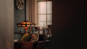A dimly lit room with a table set for dining, a decorative wall clock, and a stained glass window. - Maison Heler Metz, Curio Collection By Hilton (Metz)