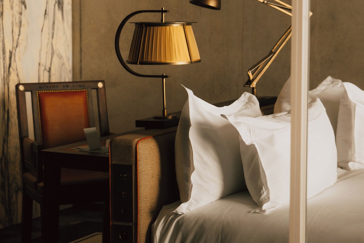 A hotel room with a bed, a desk, a chair, and a lamp.