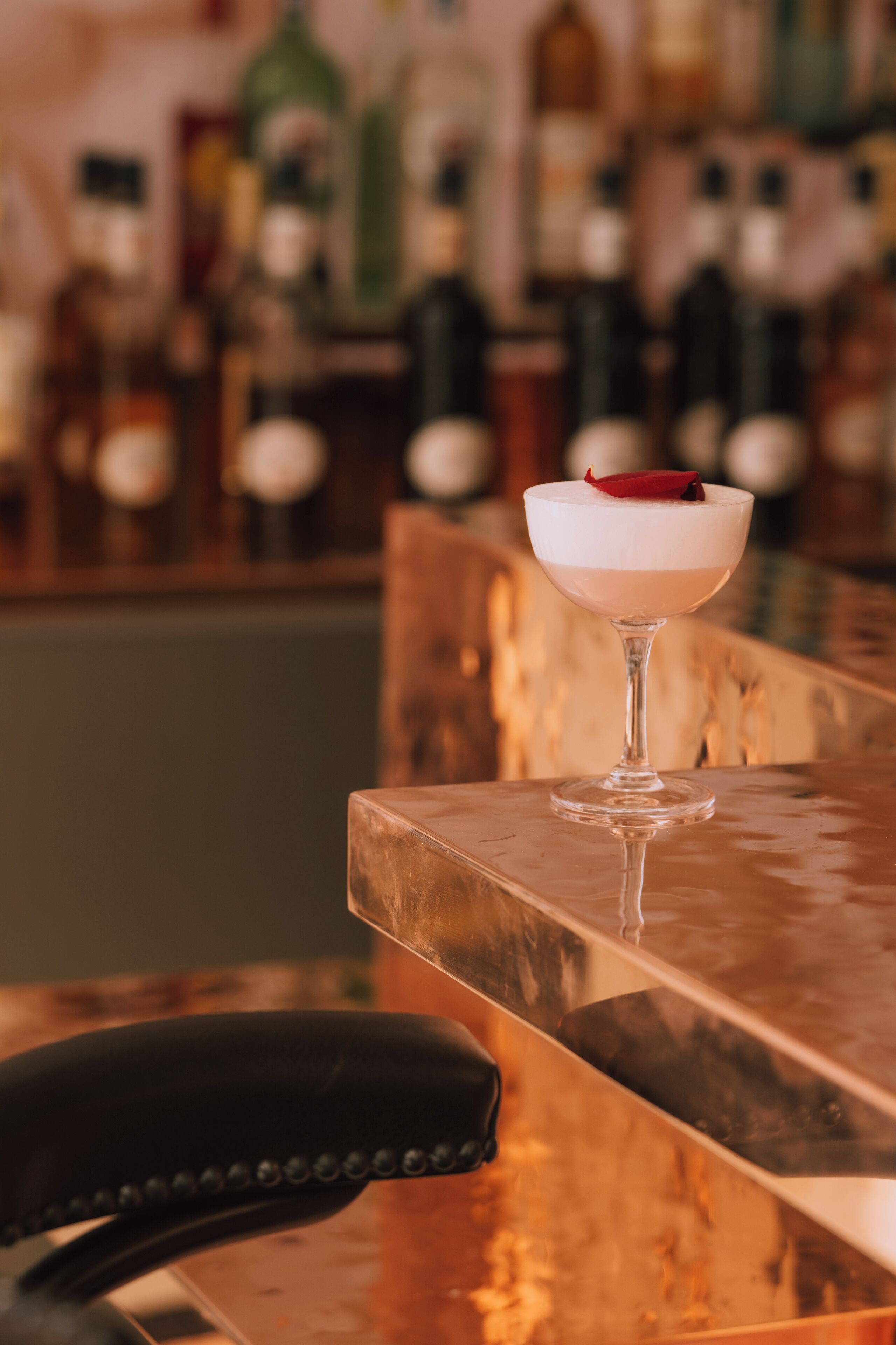 Un cóctel en un vaso sobre una barra, con un fondo desenfocado de botellas.
