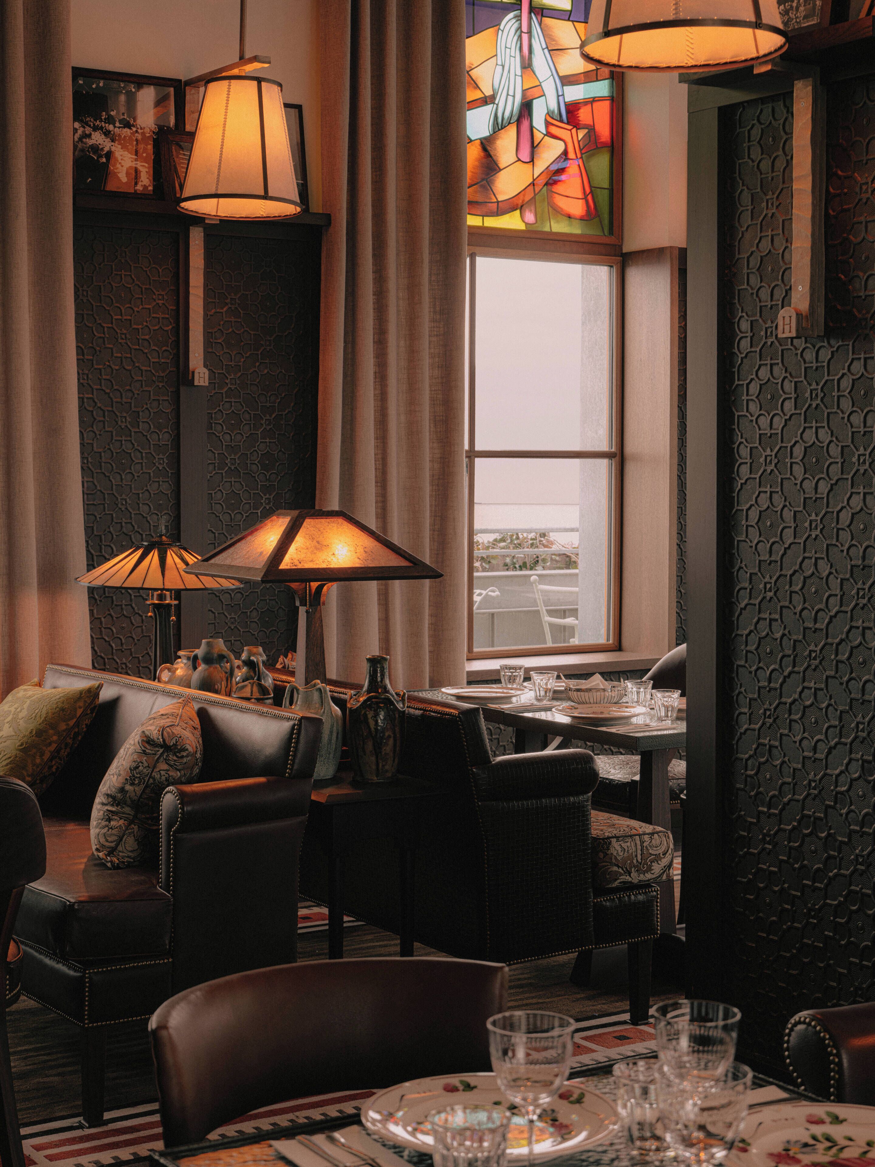 A cozy dining area with leather chairs, a table set for two, and a stained glass window in the background.