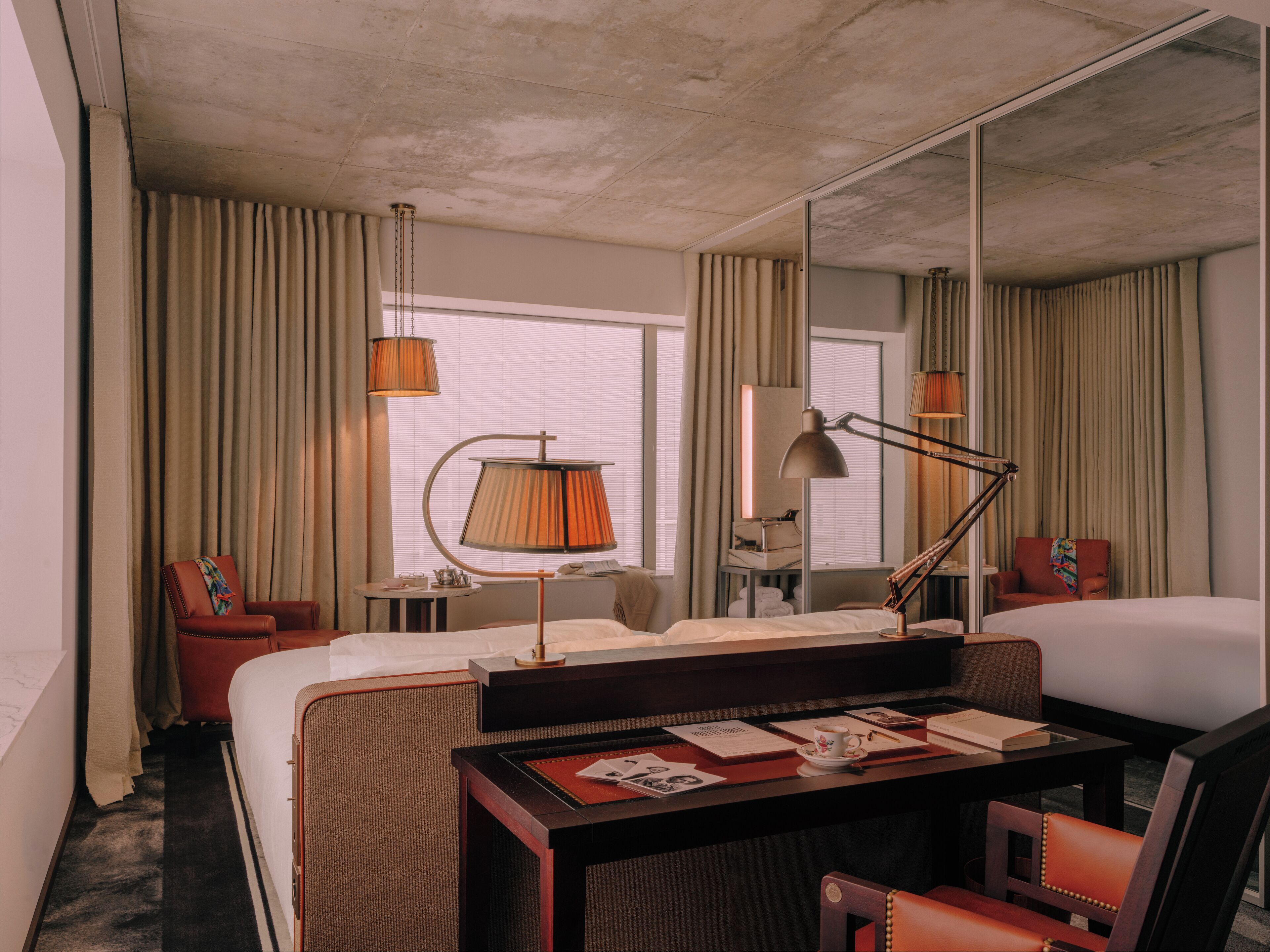 Una habitación de hotel con una cama, un escritorio con lámpara, una silla y un espejo grande.