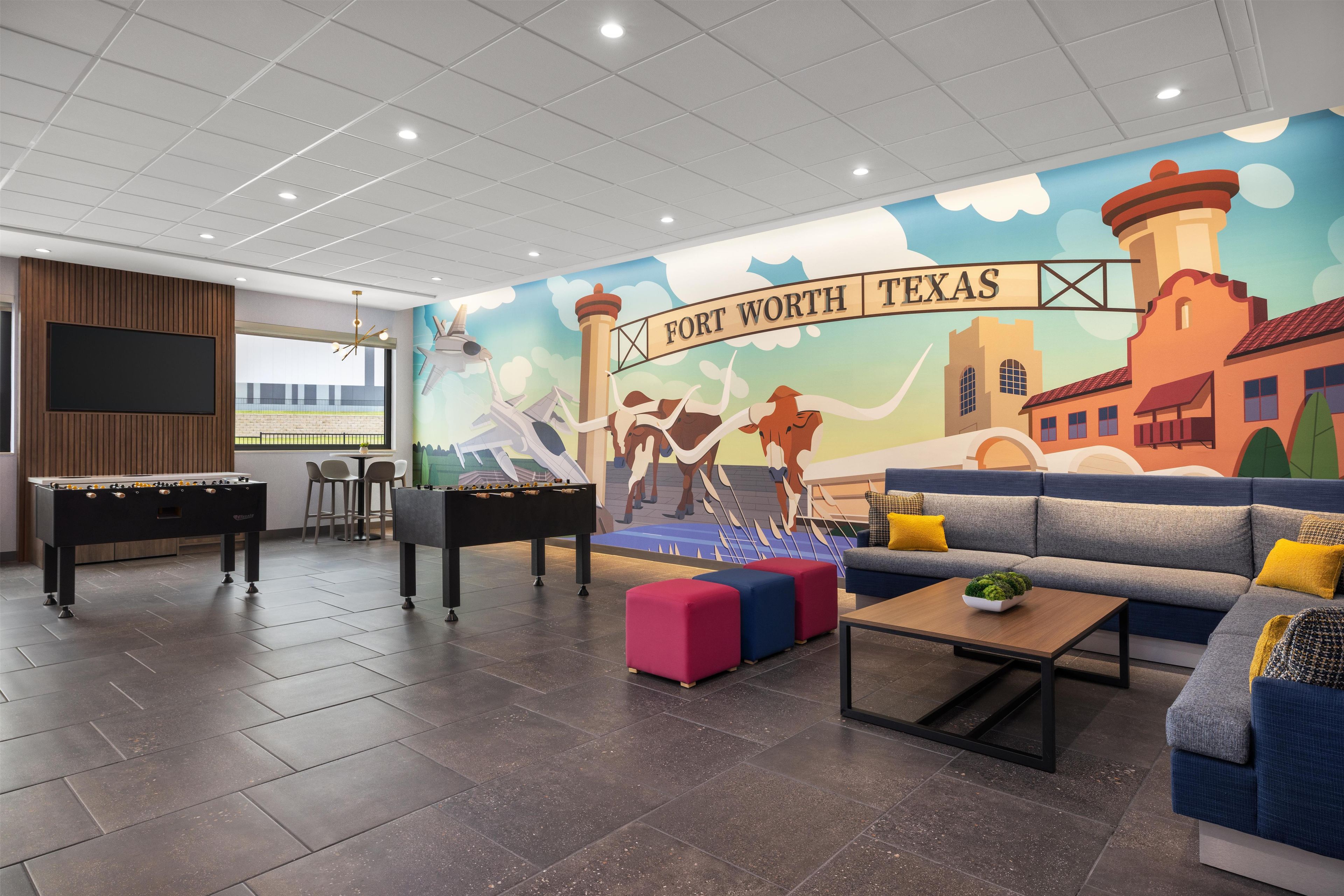 Una habitación con mesa de fútbol, sofá, otomanes y un mural de Fort Worth, Texas.