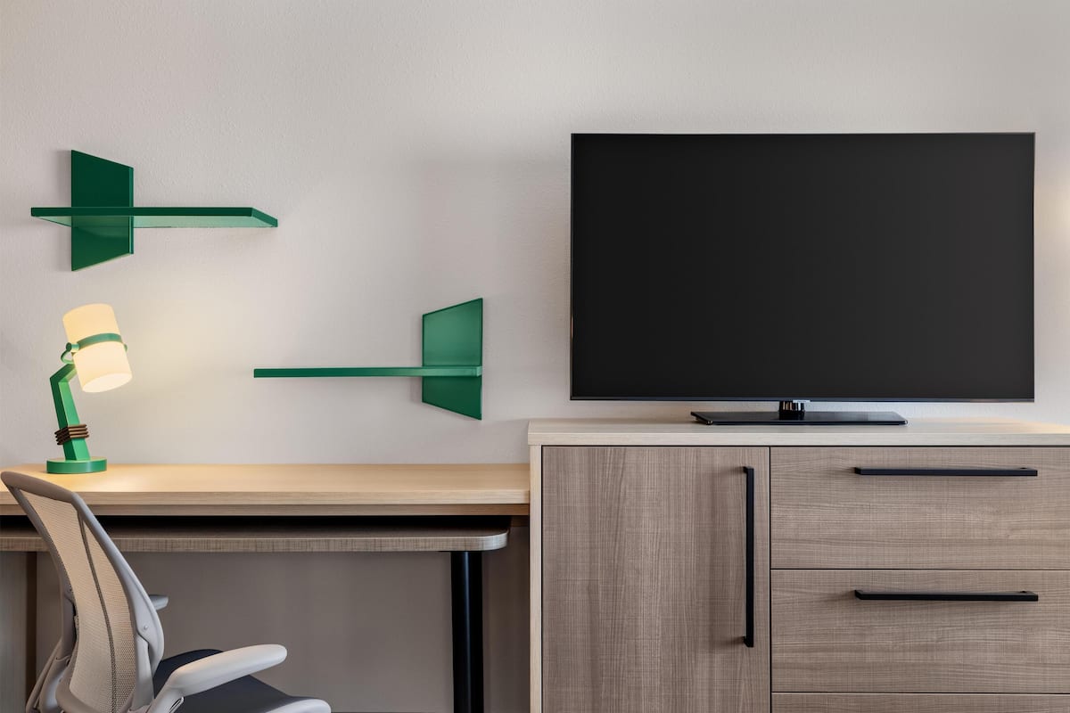 Un espace de bureau moderne comprenant un bureau, une chaise, un téléviseur et des étagères vertes fixées au mur.