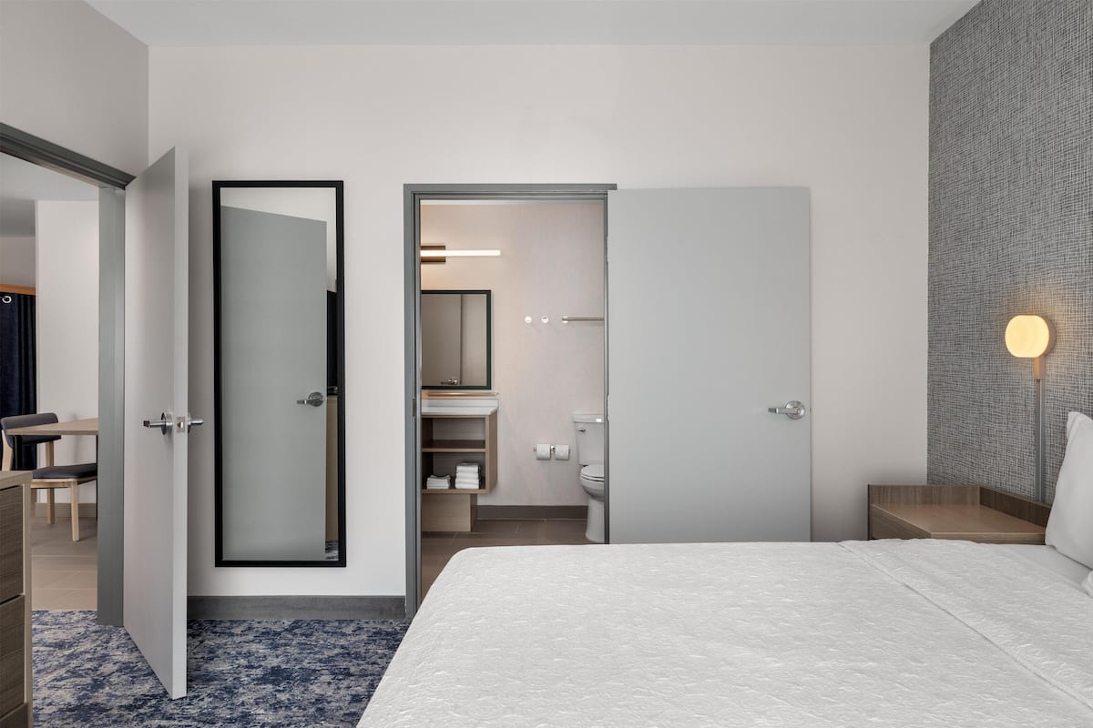 Une chambre d’hôtel moderne, dotée d’un grand lit, d’une salle de bain avec des toilettes et un lavabo, ainsi que d’un bureau avec une chaise.